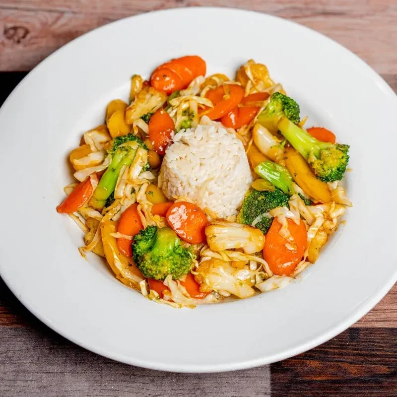 Colorful stir-fried vegetables and white rice on a round plate.