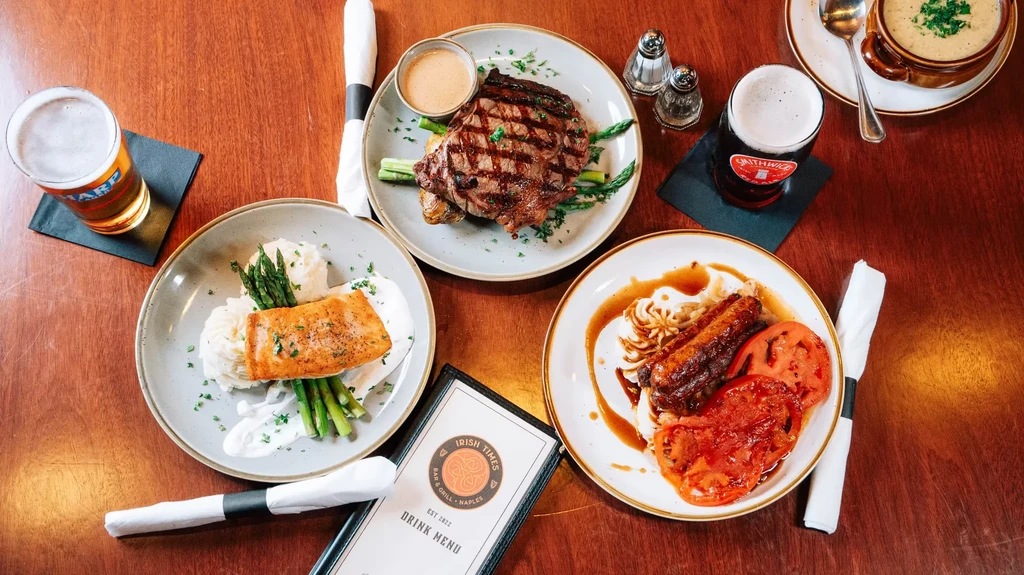 Flat lay: various hearty meals, beers, soup, and menu on table.