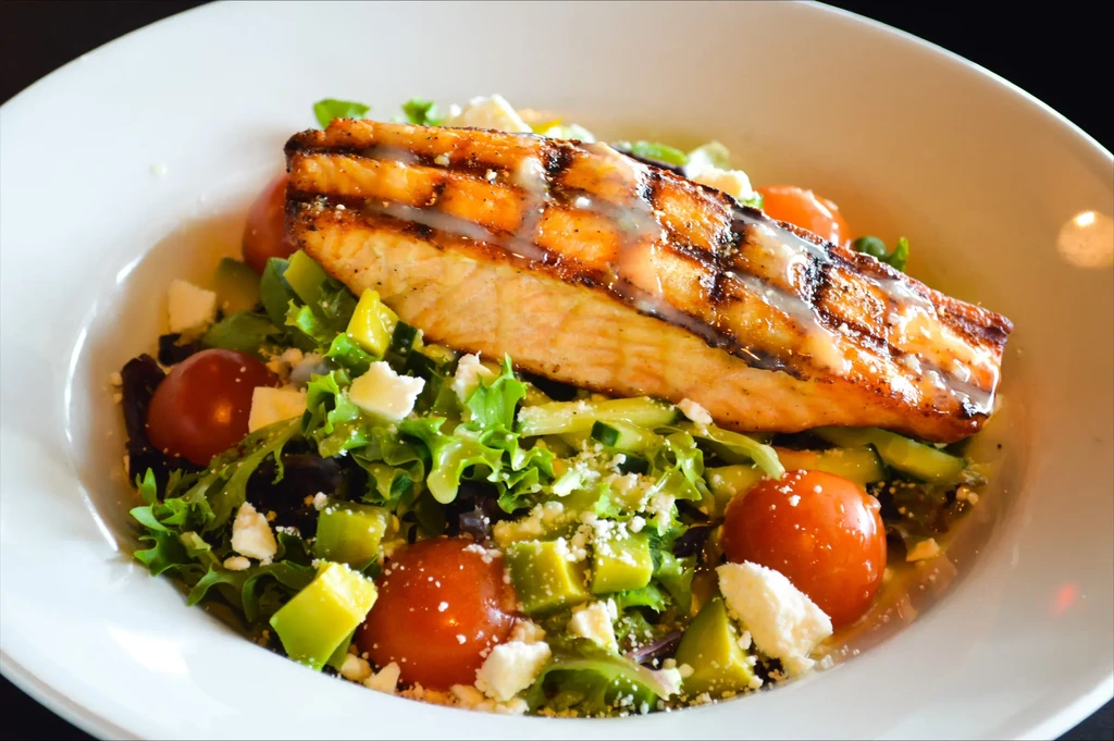 Grilled salmon fillet on a vibrant salad with avocado and feta.