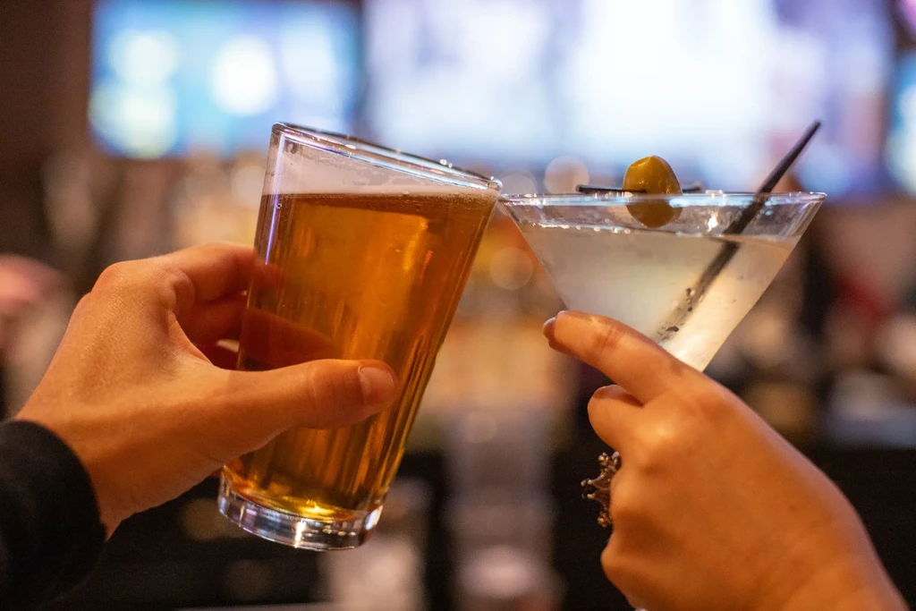Close-up of two hands toasting glasses: a beer and a martini.