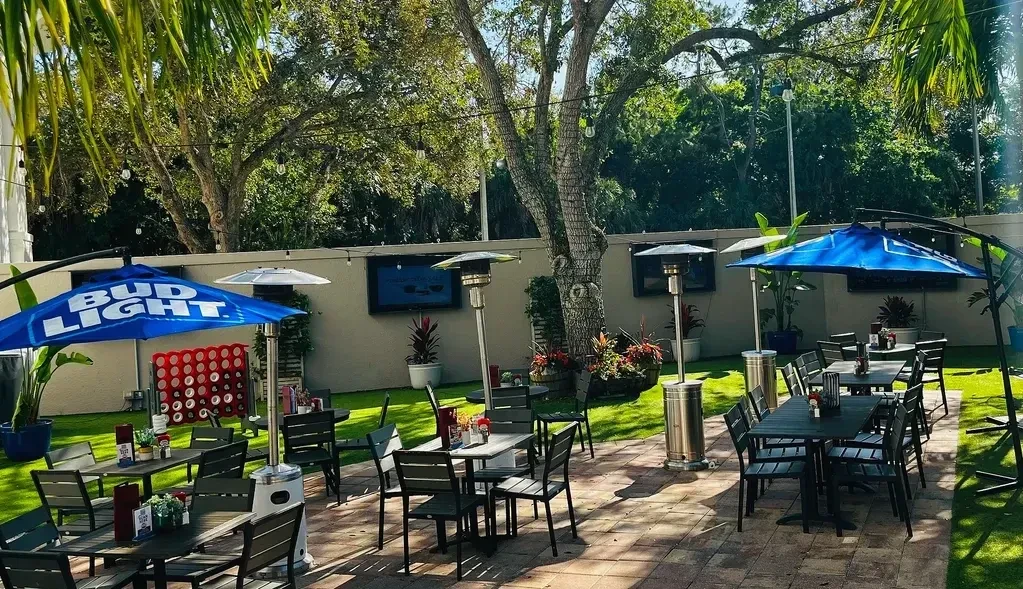 Outdoor patio with tables, umbrellas, TVs, and a large game.