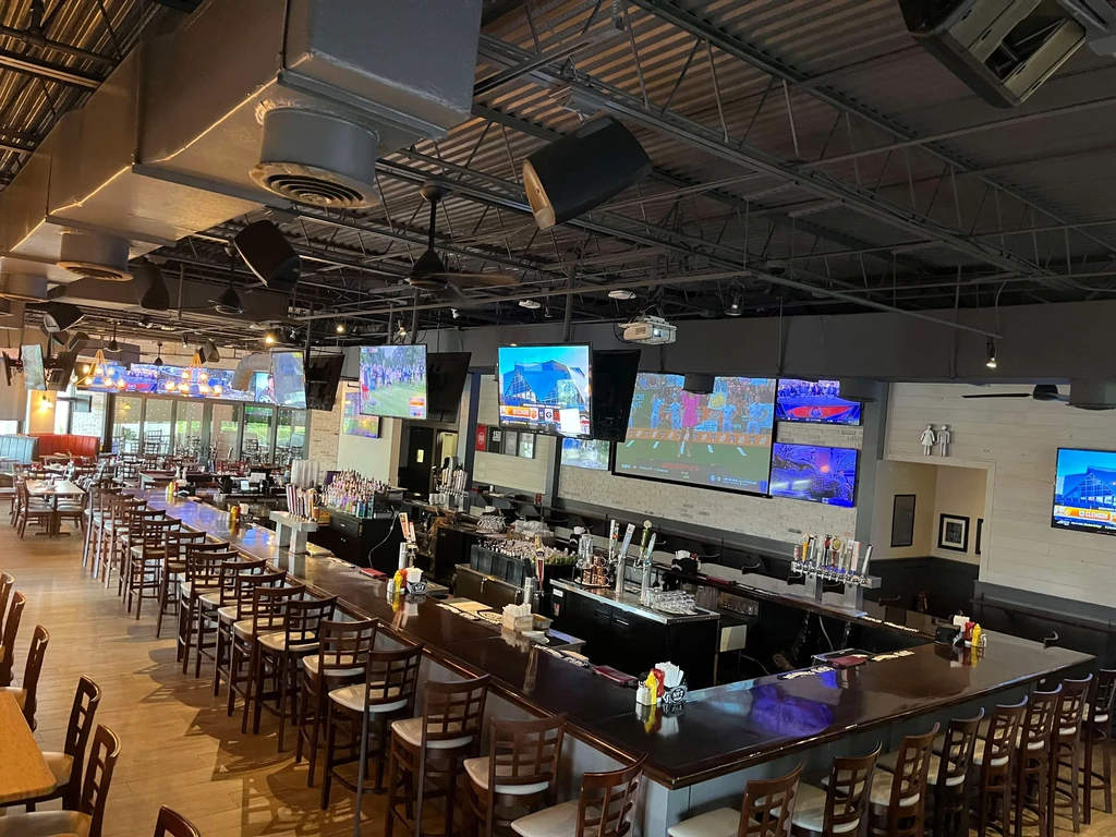 Modern sports bar with U-shaped bar, dining area, and multiple TVs.