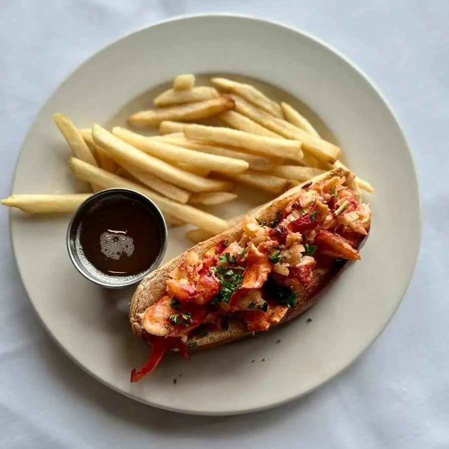 A lobster roll with french fries and a dipping sauce.