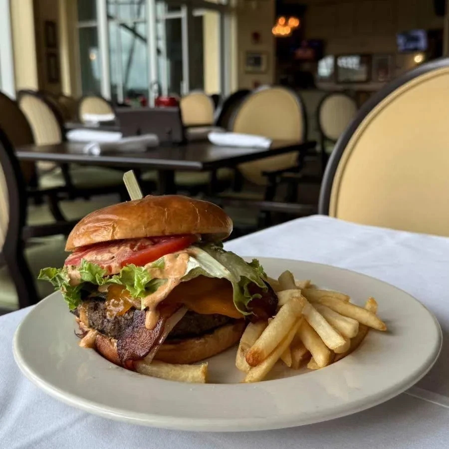 Close-up: tall gourmet burger with cheese, bacon, and golden fries.