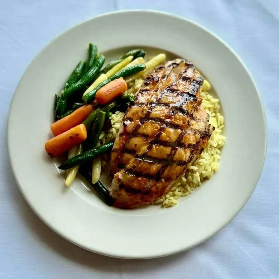 Grilled chicken with grill marks, yellow rice, green beans, and carrots.