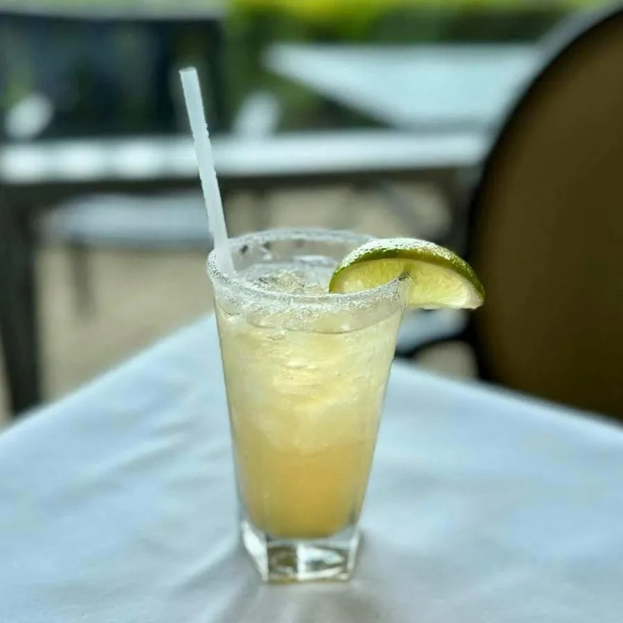 Salt-rimmed margarita in hexagonal glass with lime and straw outdoors.