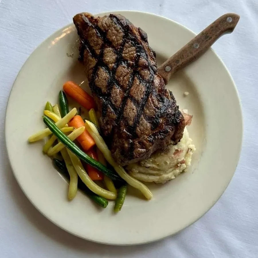 Plated grilled steak, mashed potatoes, and mixed vegetables with a knife.