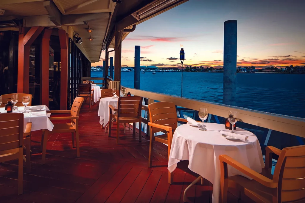 Empty outdoor dining patio overlooking water at sunset with a tiki torch.