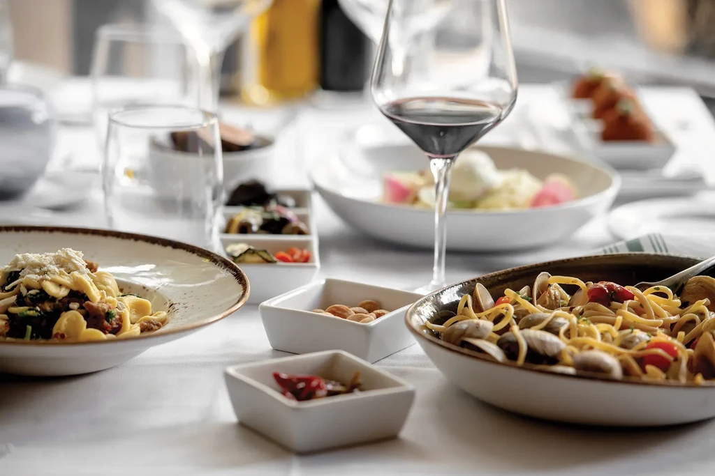 Restaurant table with various pasta dishes, red wine, and appetizers.