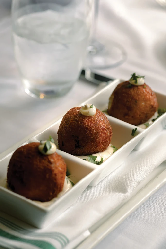 Three crispy golden-brown appetizers on sauce, garnished with herbs.