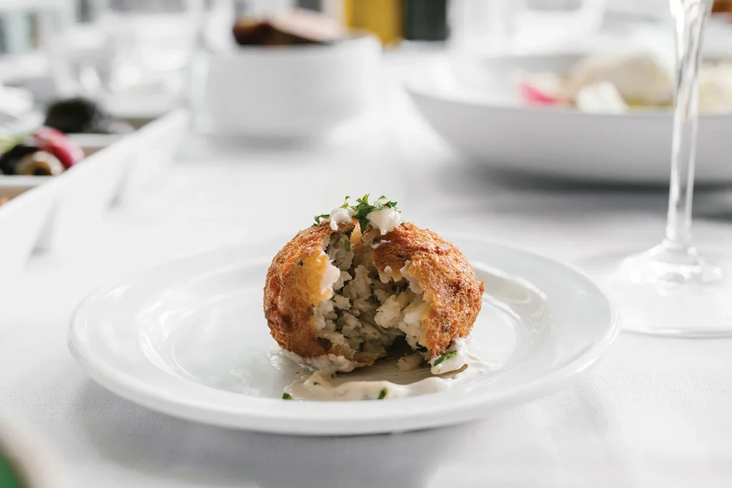 Cut-open fried arancini or croquette with sauce and herbs.