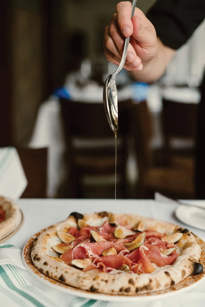 Hand drizzles gourmet fig and prosciutto pizza with liquid.