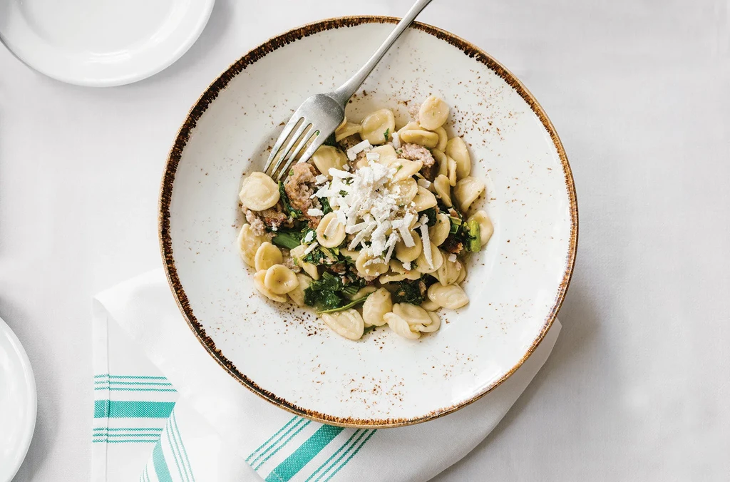 Top-down Orecchiette pasta with sausage, greens, cheese, and a fork.