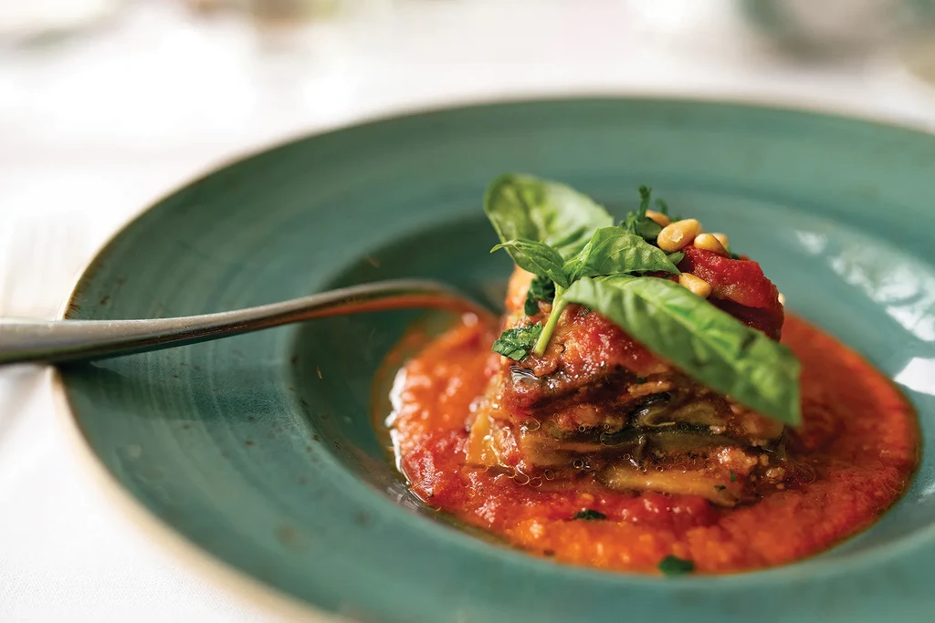 Stacked eggplant parmesan in tomato sauce, garnished with basil and pine nuts.