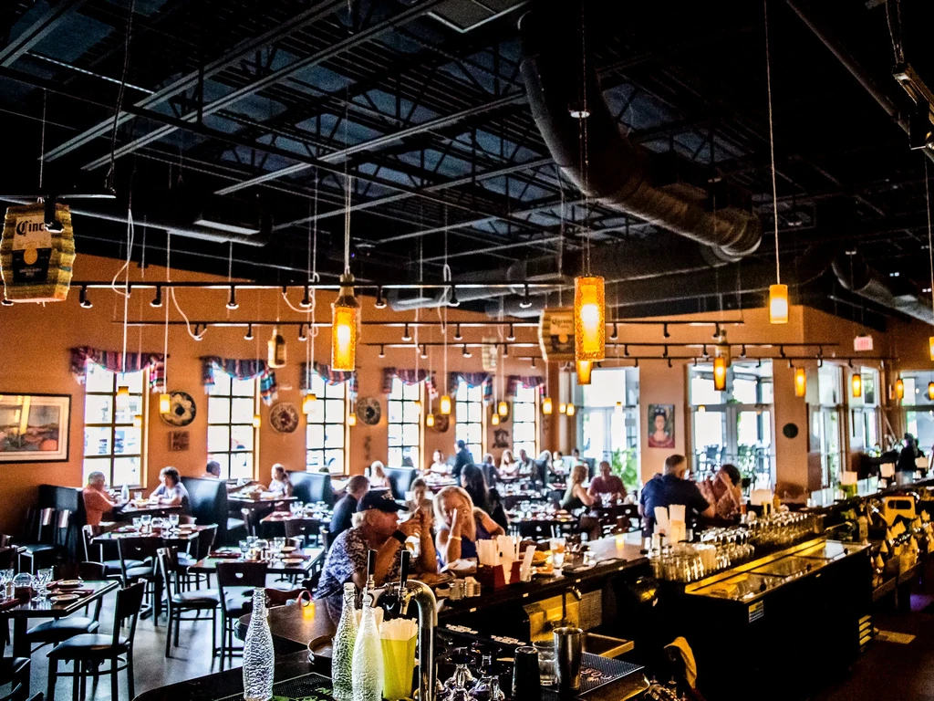 Lively, industrial-style restaurant interior with a busy bar and diners.