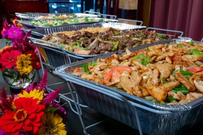 Buffet line with catering trays of chicken, beef, vegetables, and flowers.