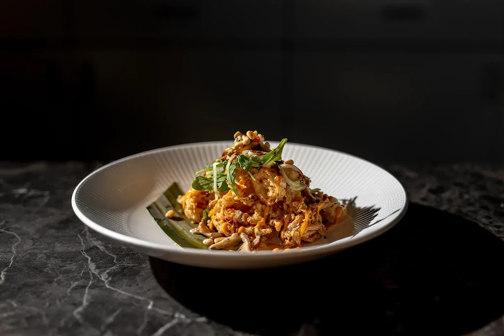 Crispy fritters with orange sauce, herbs, and nuts in a white bowl.