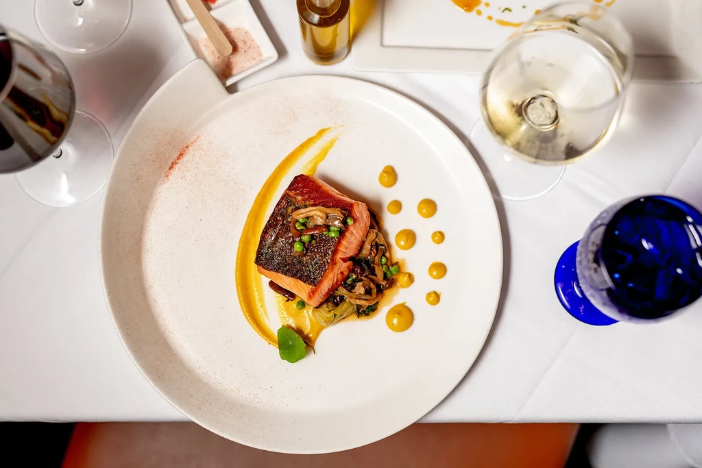 Meticulously plated seared salmon, purée, greens, and wine glasses.