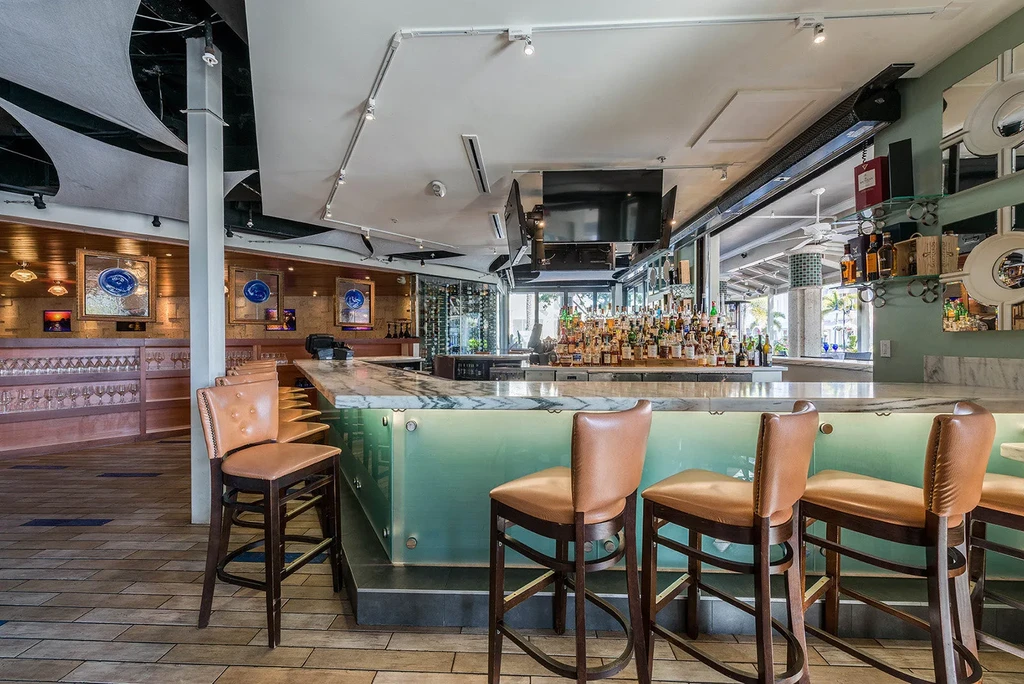 Modern bar with marble top, backlit aqua base, liquor, and palm trees.