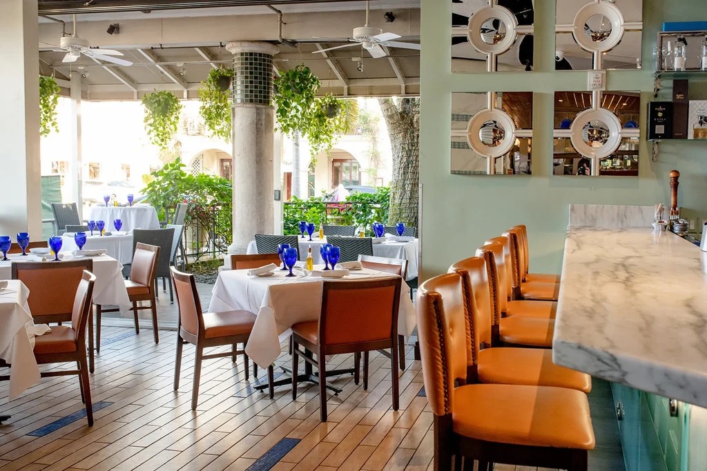 Elegant restaurant with dining tables, marble bar, blue glassware, and lush plants.
