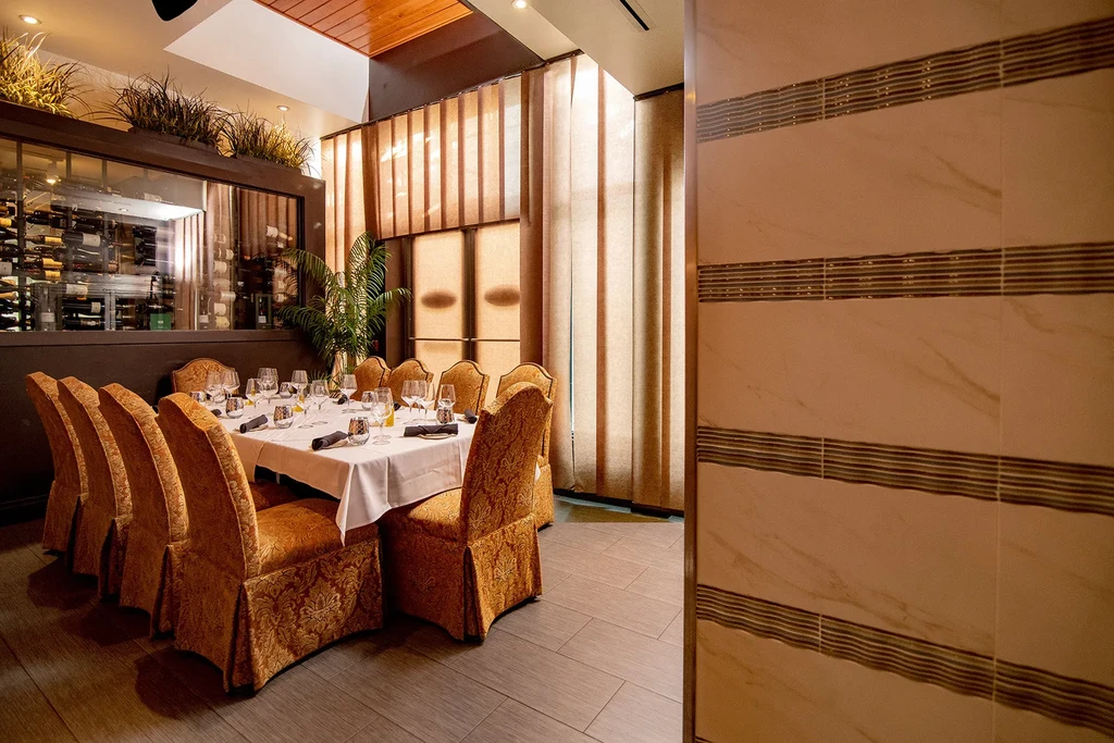 Elegant private dining room with set table, gold chairs, and wine cellar.