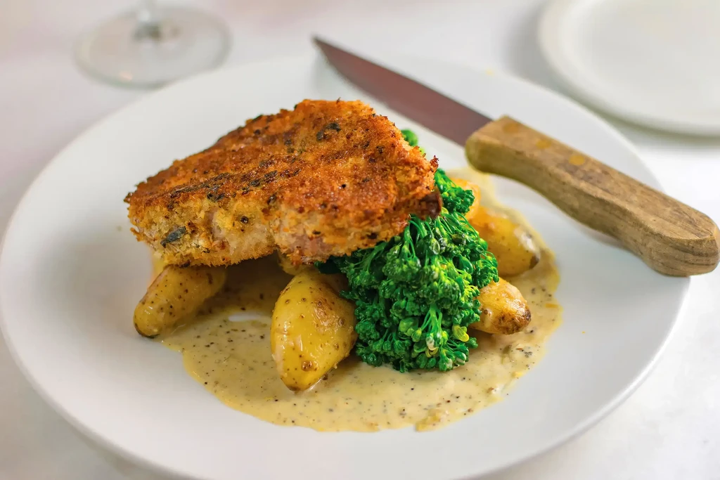 Close-up of crispy breaded cutlet, roasted potatoes, broccolini, and creamy sauce.