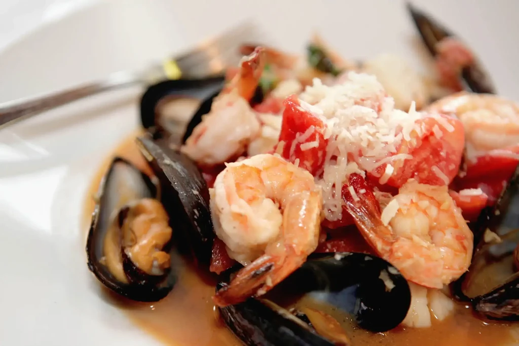 Mussels and shrimp dish with tomatoes, cheese, and orange sauce.