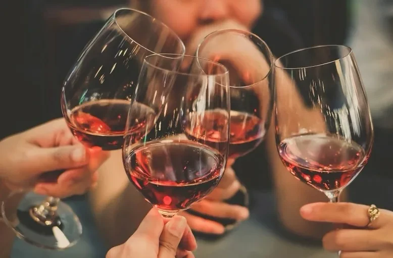 Four wine glasses filled with reddish-rosé wine clink in a toast.