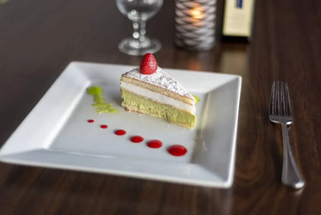 Multi-layered cake slice with strawberry, garnished, on a restaurant table.