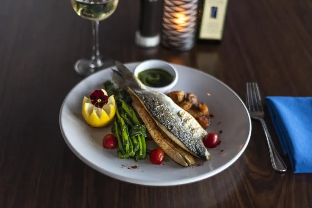 Grilled fish, blanched green vegetables, roasted potatoes, lemon on a dark table.