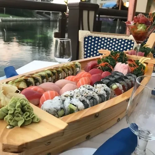 Vibrant sushi and sashimi platter with drinks and water background.