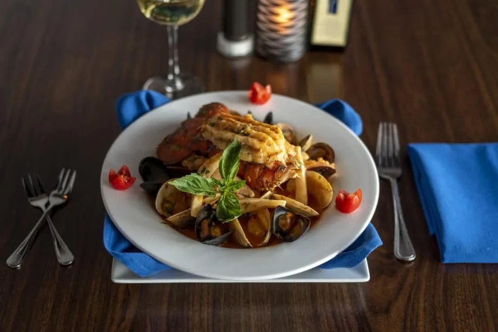 Plated seafood with lobster, mussels, pasta on an elegant table setting.