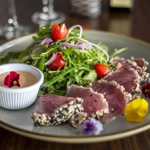 Plated seared sesame tuna, green salad, dipping sauce, and edible flowers.