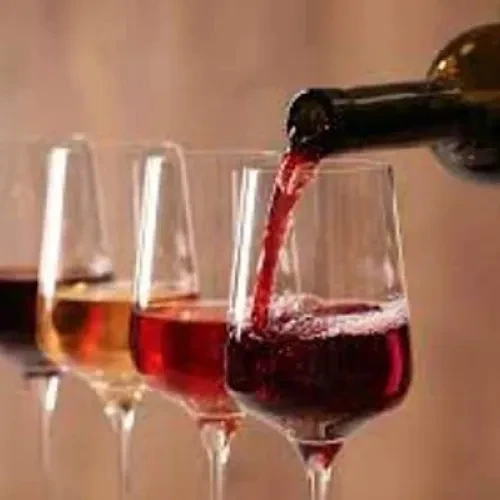 Bottle pouring red wine into glass, three other wines on display.
