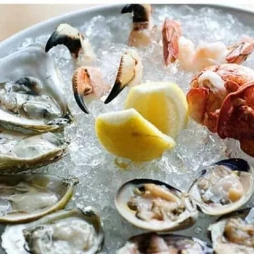 Seafood platter on ice with oysters, crab, shrimp, clams, and lemon.