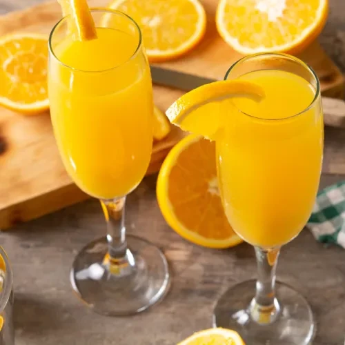 Two stemmed glasses of orange juice with orange slices, scattered fresh oranges.