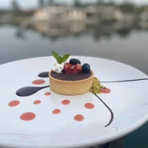 Chocolate tart topped with cream, berries, and mint on a garnished plate.