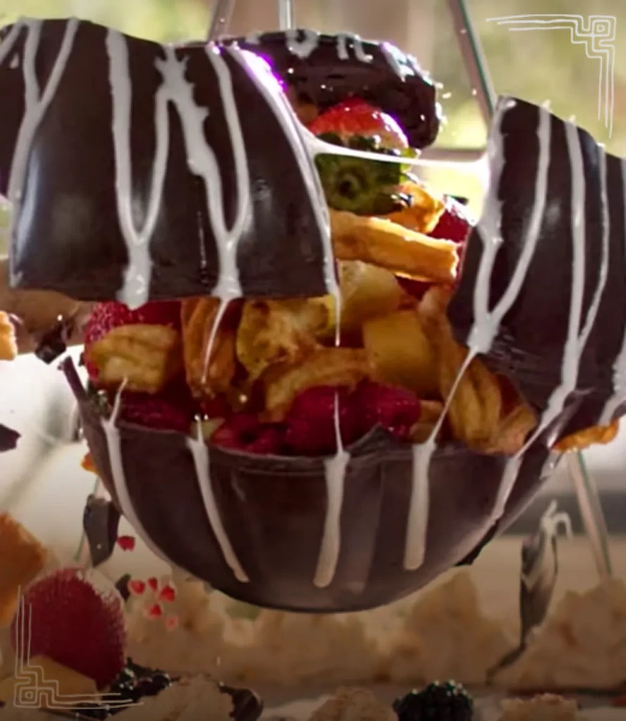 Broken chocolate sphere with white icing revealing colorful contents.