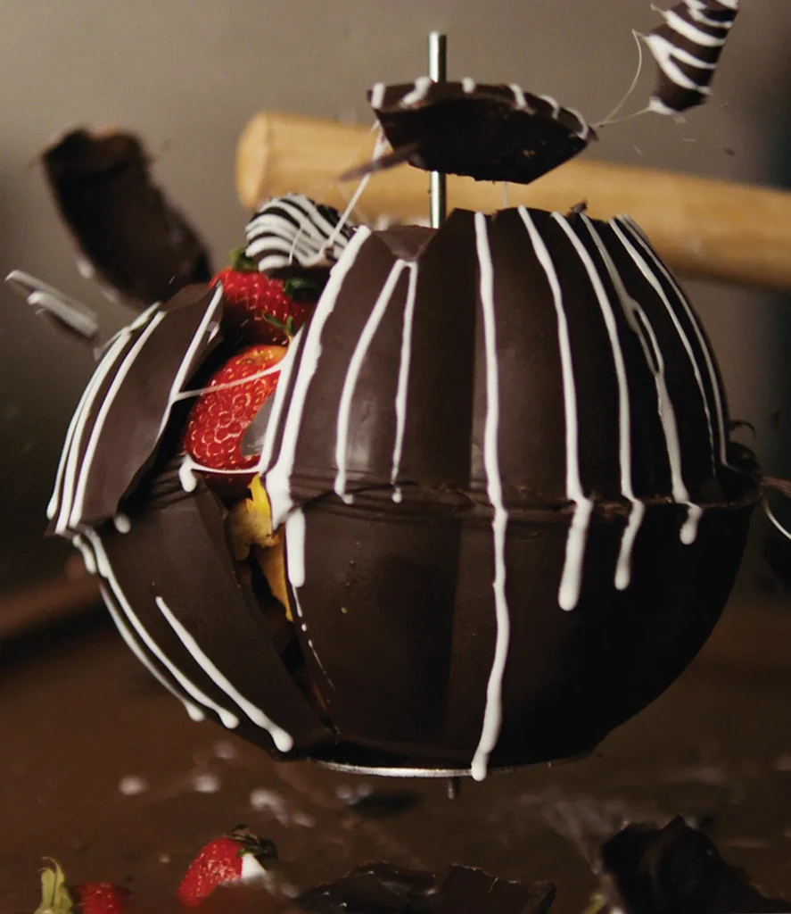 White-striped chocolate sphere shatters, revealing strawberries and yellow filling.