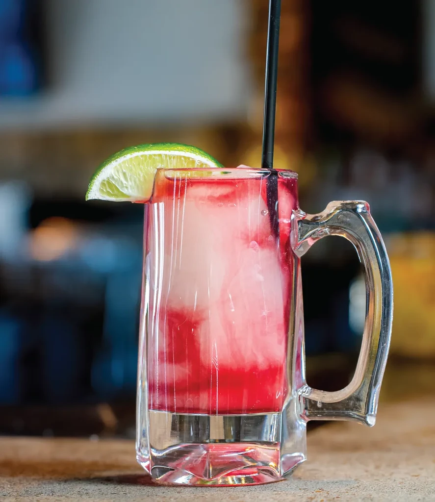 Layered pink and red drink in mug with lime and straw.