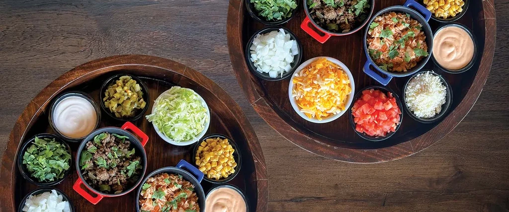 DIY taco and burrito bar with various ingredients on wooden trays.