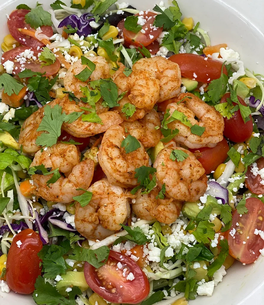 Overhead: Colorful shrimp salad with vegetables, avocado, and cheese in white bowl.