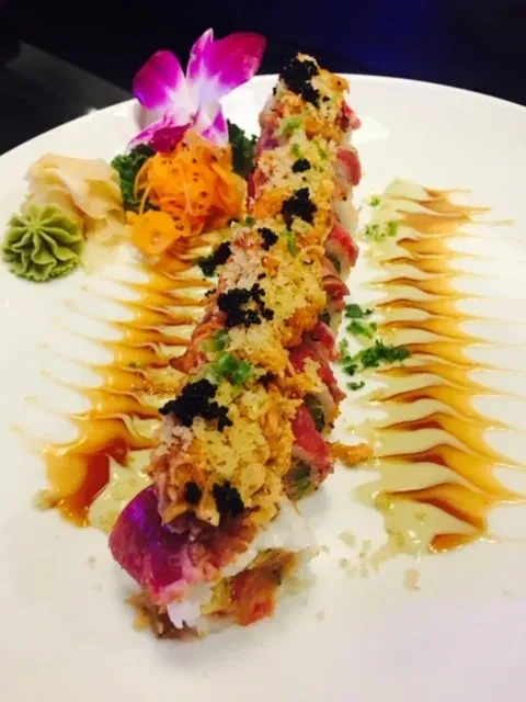 Artfully presented sushi roll with fish, roe, flakes, and decorative sauces.