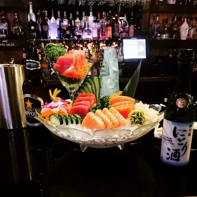 Sashimi platter with tuna, salmon, beer, and sake on a bar.