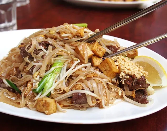 Close-up of Pad Thai with beef, tofu, and chopsticks.