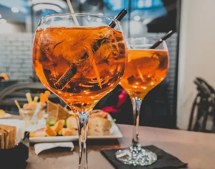 Two amber cocktails with ice and appetizers on a wooden table.