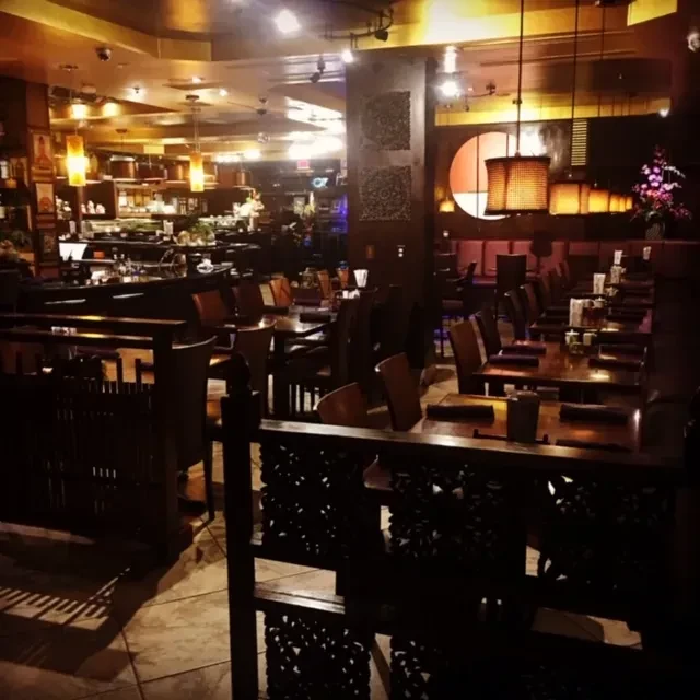 Warm, dimly lit restaurant interior with wooden tables, a bar, and dividers.