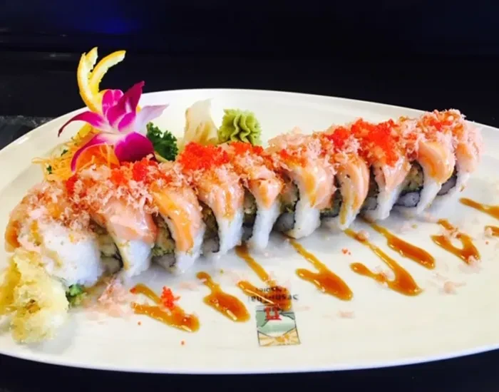 Plated sushi roll with salmon, tobiko, tempura, orchid, ginger, and wasabi.