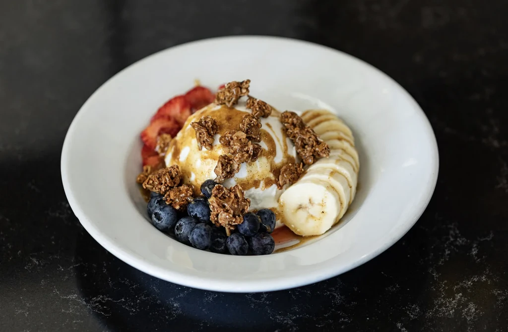 White bowl with creamy base, granola, strawberries, blueberries, and bananas.