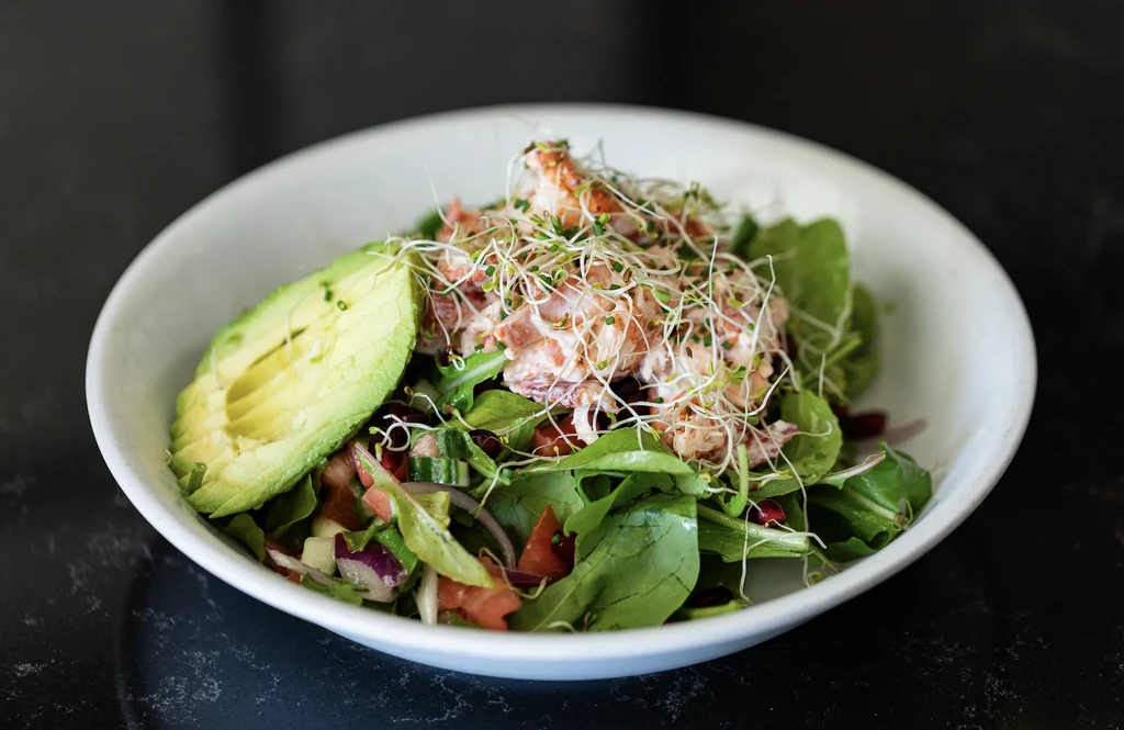 Top-down view of a fresh salad with greens, avocado, creamy protein, sprouts.